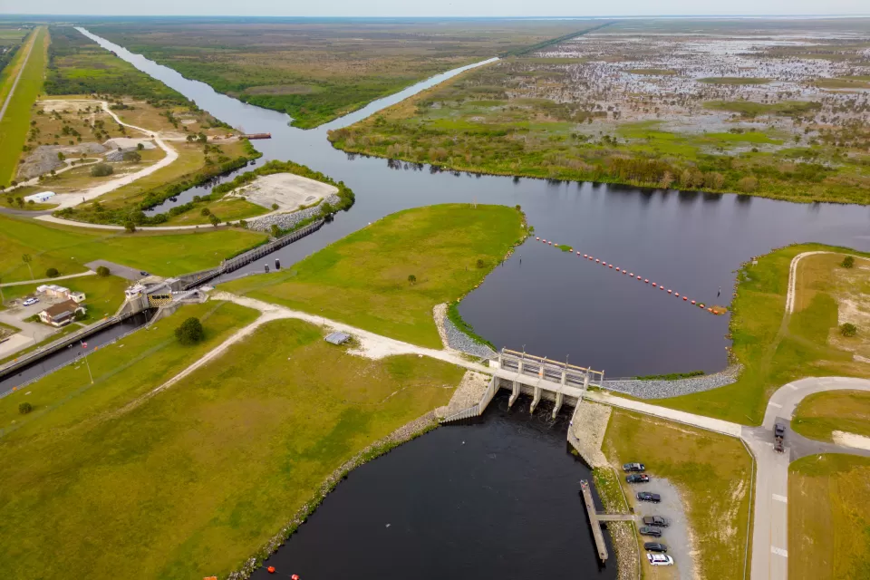 An aerial view of a lock and dam between two waterways with miles of marshes into the background of the image.